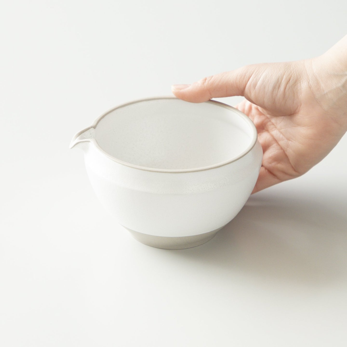 The original white ORIGAMI matcha bowl held in one hand, showing its curved rim and pouring spout